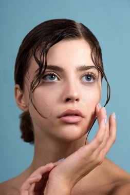 Temiz cildine ve su damlasına sahip genç ve güzel bir kadın yüzüne dokunuyor. Güzellik modelinin doğal çıplak makyajlı portresi cildini losyonla nemlendiriyor. Spa, cilt bakımı ve sağlık. Kapat, arkaplan, kopyala.