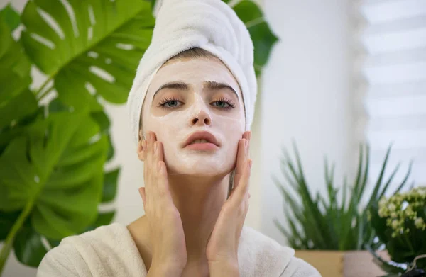 Young woman applying face mask on her face. Beauty model with  perfect fresh skin and long eyelashes cares about her skin at home or beauty salon. Spa and Wellness, Skin Care Concept. Close up, selected focus.