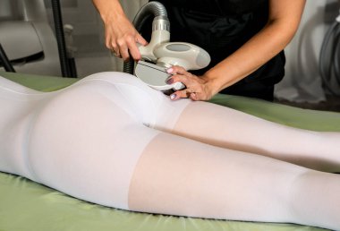 Beyaz takım elbiseli kadın güzellik salonunda selülit karşıtı masaj yaptırıyor. LPG, ve klinikte vücut şekillendirme tedavisi. Kadın vücudunda lipomasaj prosedürü. Vücut bakımı.