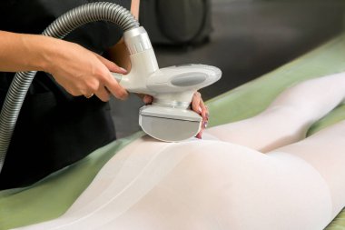 Beyaz takım elbiseli kadın güzellik salonunda selülit karşıtı masaj yaptırıyor. LPG, ve klinikte vücut şekillendirme tedavisi. Kadın vücudunda lipomasaj prosedürü. Vücut bakımı.