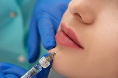 Kozmetik uzmanının elleri yüzüne ve dudaklarına iğne yapıyor. Genç bir kadın güzellik salonunda yüz aşısı yaptırıyor. Yaşlanma, gençleşme ve hidrasyon prosedürleriyle yüzleş. Estetik kozmetoloji. Kapat..