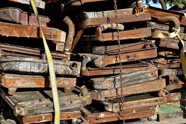 Stacks of rusty radiators from old autos and trucks are piled on a trailer