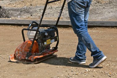 Bir adam somut bir proje üzerinde kum kompakt için titreşimli bir makine kullanır