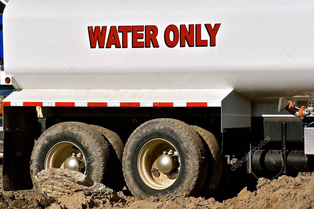 A water truck for construction use is backed into a muddy setting