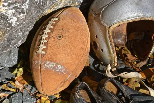 An old leather football, helmet and a pair of cleated shoes shoes bring back  the autumn memories of a past era of the gridiron.