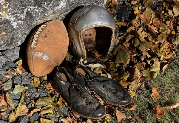 An old leather football, helmet and a pair of cleated shoes shoes bring back  the autumn memories of a past era of the gridiron.