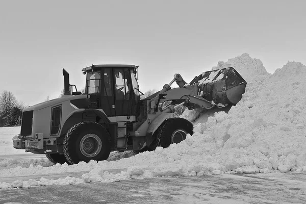 A four wheel drive tractor uses a hydraulic scoop to pile a hug snow mound.