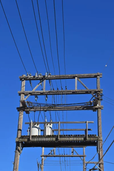 A series of high line wires and transformers run through an alley.