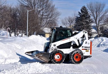 MOORHEAD, MINNESOTA, February 20, 2019: The S650 Bobcat skid steer removing driveway snow is headquartered in West Fargo, North Dakota. clipart