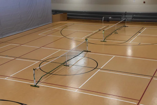 Overhead spotlights reflect off the floor of an interior pickle ball court.