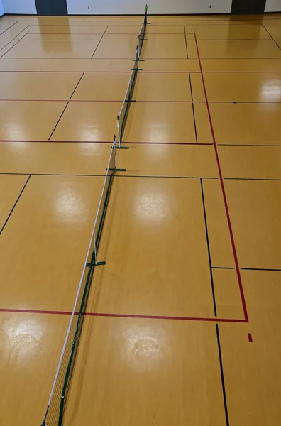 Overhead spotlights reflect off the floor of an interior pickle ball court.
