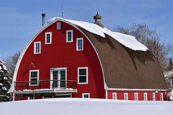 Snow on the roof of an old red rounded barn is in the first stage of melting