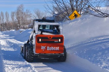 MOORHEAD, MINNESOTA, March 9, 2019: The S650 Bobcat skid steer removing driveway snow is headquartered in West Fargo, North Dakota. clipart