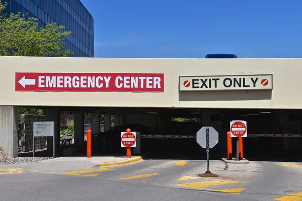 A parking ramp  displays exit signs next to a hospital with a sign indicating location of the emergency center