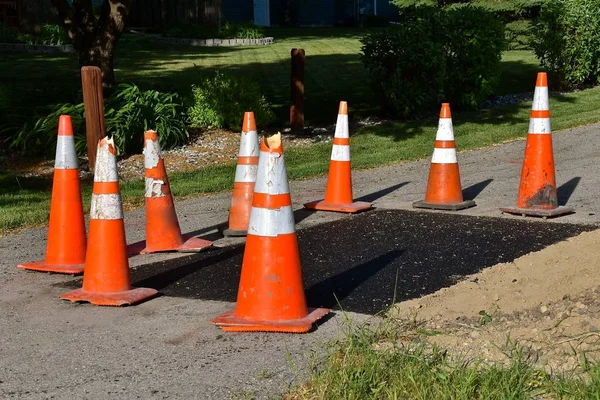 Orange warning cones surround an asphalt repair job on a sidewalk bike path.