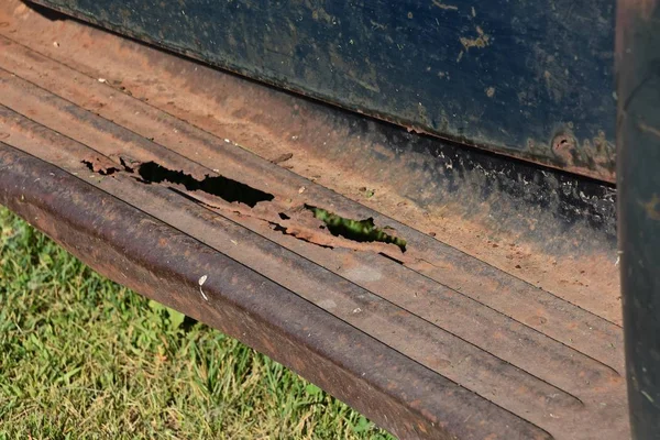 The running board of a n old rusty pickup is full of corroded holes.