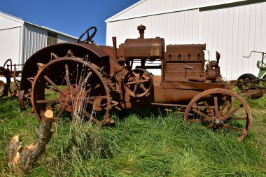 The unidentifiable rusty old tractor on steel wheels is missing  many parts