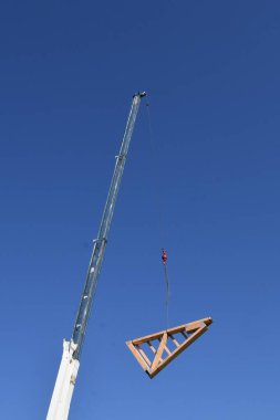 Önceden inşa edilmiş kirişler bir kabloyla kaldırılıyor ve inşaat halindeki ahşap çerçeveli bir binanın tepesine yerleştiriliyor..