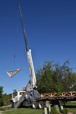 Önceden inşa edilmiş kirişler bir kabloyla kaldırılıyor ve inşaat halindeki ahşap çerçeveli bir binanın tepesine yerleştiriliyor..