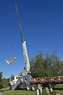 Önceden inşa edilmiş kirişler ve kirişler bir kablo tarafından kaldırılıyor ve inşaat halindeki ahşap çerçeveli bir binanın tepesine yerleştiriliyor..
