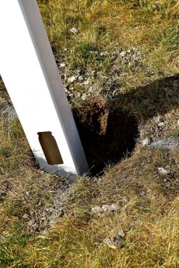 Arka bahçe mahremiyeti için beyaz bir vinil direği nihai yerleştirme için betonu bekliyor.. 