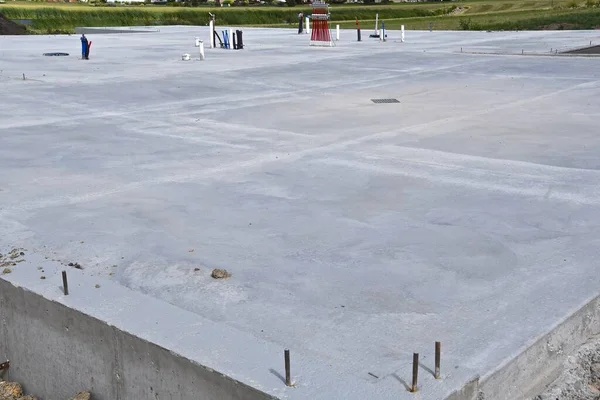 A freshly poured concrete pad for a house without a basement which displays plumbing, water, lines, and anchor rods.