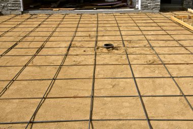 Güçlendirme çubukları, yakında beton elde etmek üzere gelecekteki bir garaj yolunun kumları üzerinde kare desen oluşturur.