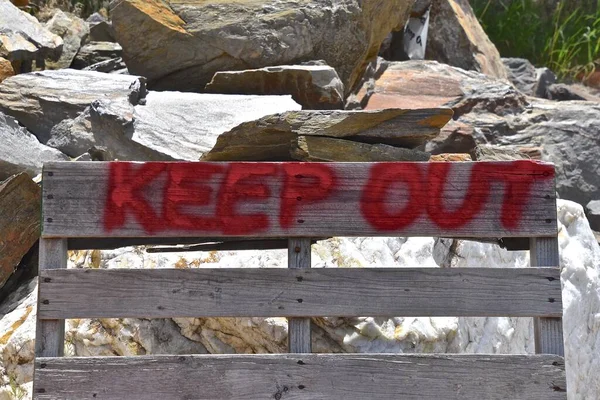 KEEP OUT sign has been spray painted red on an old red wood pallet.