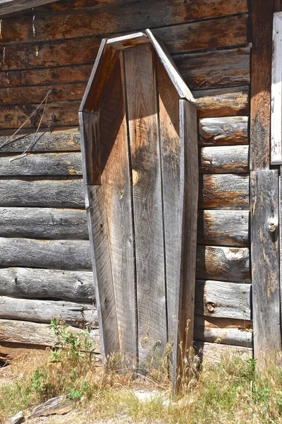在旧的西部 一个装尸体的棺材笔直地立在一个生机勃勃的旧木屋前 — 图库照片