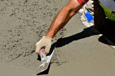 Bir duvar ustası, ıslak çamur itilip düzleştirilirken el ele tutuştuğu malayla betonu düzleştiriyor..