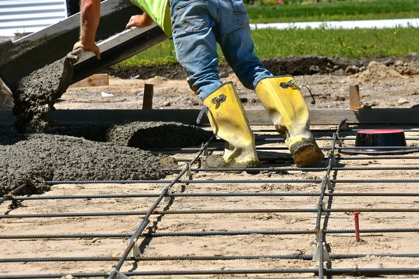 A construction worker with boots is working with wet mud as it comes down the chute of a ready-mix truck.