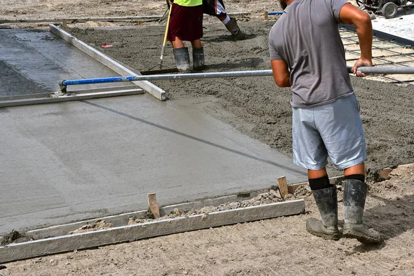 A cement worker uses the bull float to level and smoothen fresh concrete poured on a new driveway.