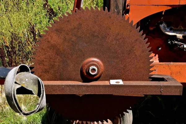 A huge rusty saw blade is mounted on a tractor with a leather belt to be attached to the belt pulley for power