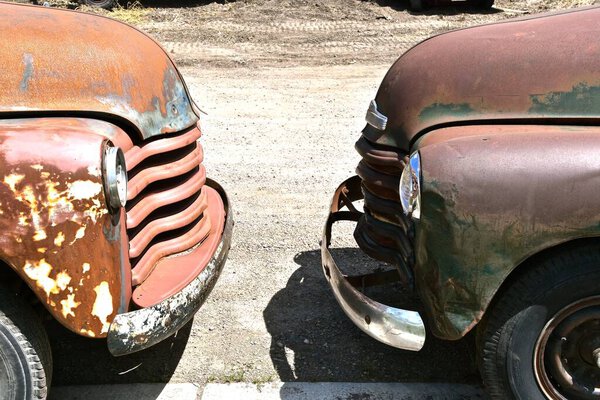 The front bumpers of two old rusted pickups are nearly touching.