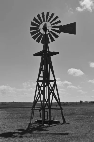 An old windmill is silhouetted against the sky in a prairie setting. (black and white)