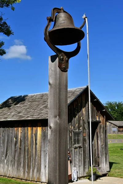 プルロープ付きの鋳鉄製の鐘は 古い歴史的な復元された古い1つの部屋の校舎の前にあります — ストック写真
