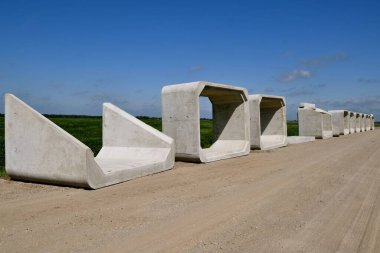 Yeni menfez olarak kullanılacak büyük beton bölümler çakıllı yolda bir hat üzerinde yer almaktadır.