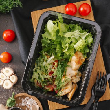 Ahşap tahta üzerinde marul ve roka siyah kase ile ızgara tavuk üstten görünüm