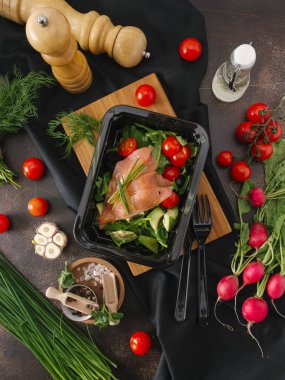 Somon, kiraz domates ve sebze ve mutfak eşyaları ile tabloda siyah tepsisinde roka salatası