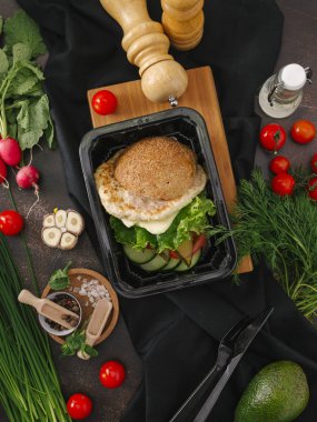 Tavuk Pirzola, marul ve sebze salatası sebze ve mutfak eşyaları ile tabloda siyah tepsisinde burger gıda kompozisyonu