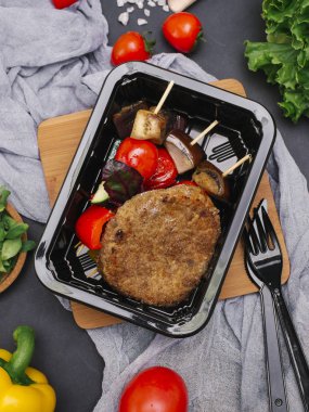 Çatal ve bıçak ile et pirzola şiş içinde siyah tepsi üzerinde ızgara sebzeler ile tedavi 