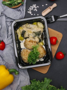 Karanlık tablo üzerinde pişmiş et pirzola ve kabak sebze ve çatal bıçak takımı ile siyah tepsisinde üstten görünüm