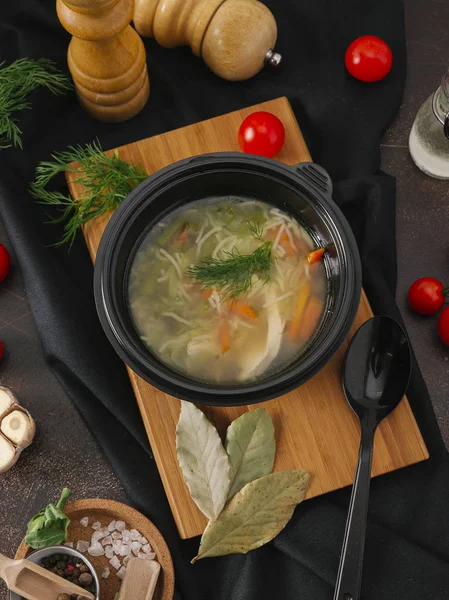 Noodle soup with vegetables and chicken in black bowl