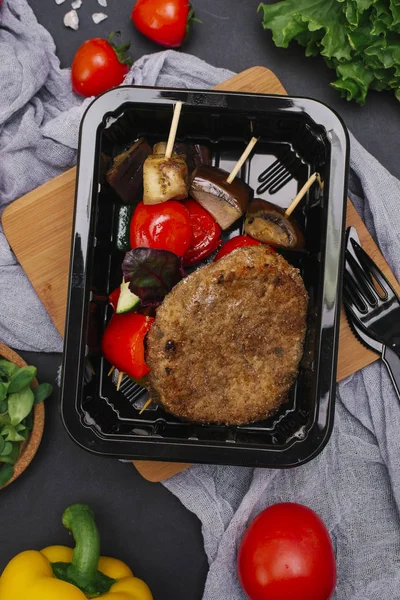 Ekmekli et pirzola şiş çatal ve bıçak siyah tepsisinde üzerinde ızgara sebzeli closeup 