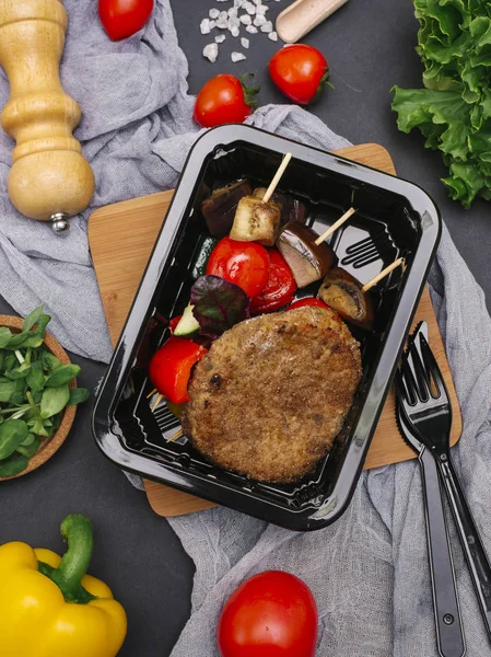 Çatal ve bıçak ile et pirzola şiş içinde siyah tepsi üzerinde ızgara sebzeler ile tedavi 