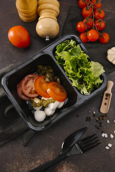 Bıçak ve çatal ahşap tahta üzerinde siyah tepsisinde Caprese salatası