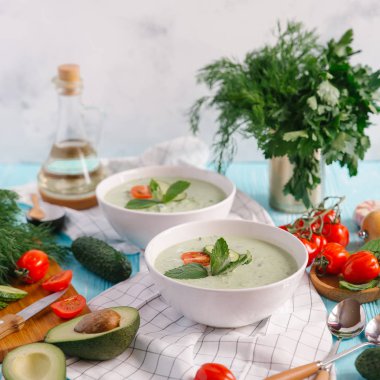 Avokado çorbası domates ve salatalık mavi ahşap zemin üzerine krem ile iki kase