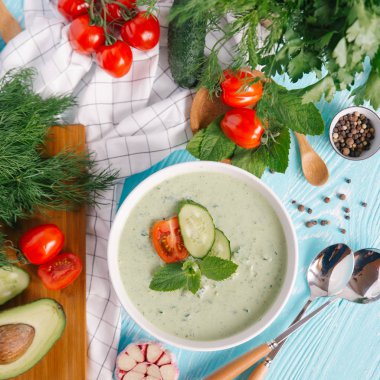 Avokado çorbası domates ve salatalık mavi ahşap zemin üzerine krem ile kase