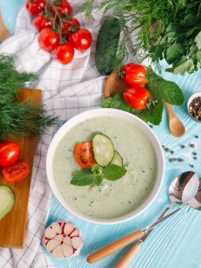 Avokado çorbası domates ve salatalık mavi ahşap zemin üzerine krem ile kase