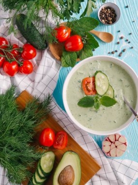 Avokado çorbası domates ve salatalık mavi ahşap zemin üzerine krem ile kase